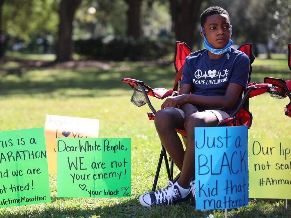 Zyon Thorpe is surrounded by signs in support of Ahmaud Arbery outside of the Glynn County Courthouse during a rally on Saturday.