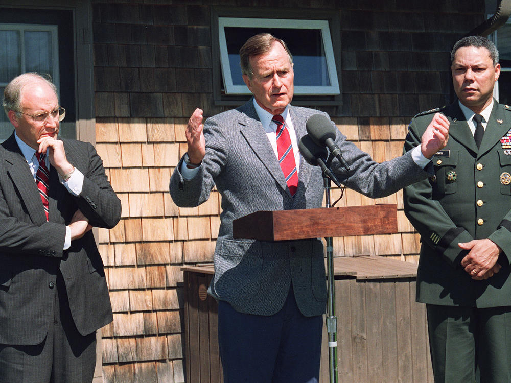 President George H.W. Bush addresses reporters on Aug. 22, 1990, in Kennebunkport, Maine, flanked by Defense Secretary Dick Cheney (L) and Chairman of the Joint Chiefs of Staff Gen. Colin Powell, following a meeting dedicated to the military situation in the Gulf.