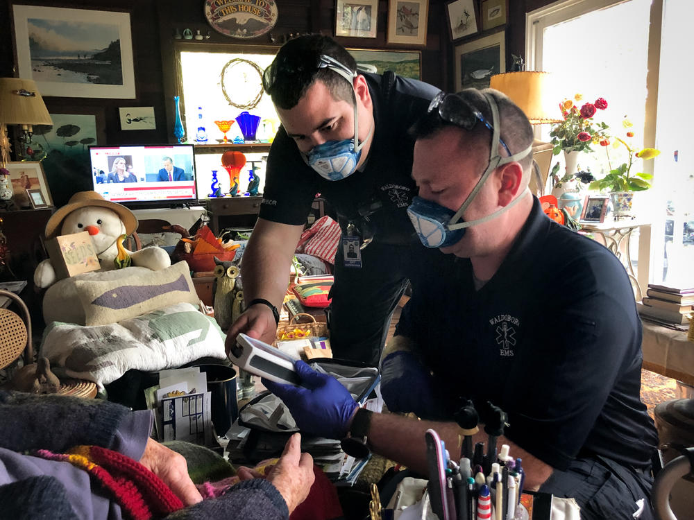 In between answering 911 calls, Jerrad Dinsmore (left) and Kevin LeCaptain perform a wellness check at the home of a woman in her nineties. The ambulance team in the small town of Waldoboro, Maine was already short-staffed. Then a team member quit recently, after the state mandated all health care workers get the COVID-19 vaccine.