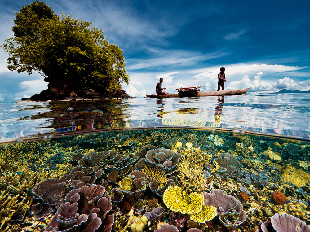 A fisherman sails with his son in an outrigger. They live in a village on the Willaumez Peninsula on New Britain Island, Kimbe Bay, Papua New Guinea.