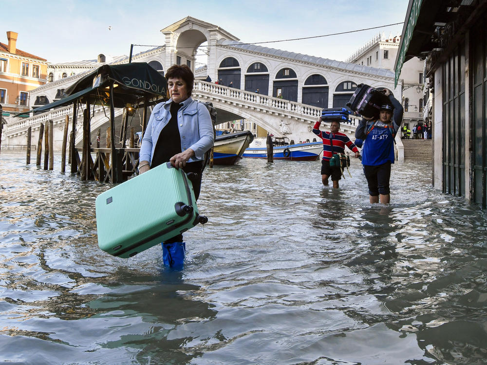 In this Dec. 23, 2019 file photo, people carry their luggage as they wade through water during a high tide of 1.44 meters (4.72 feet), near the Rialto Bridge, in Venice, Italy.