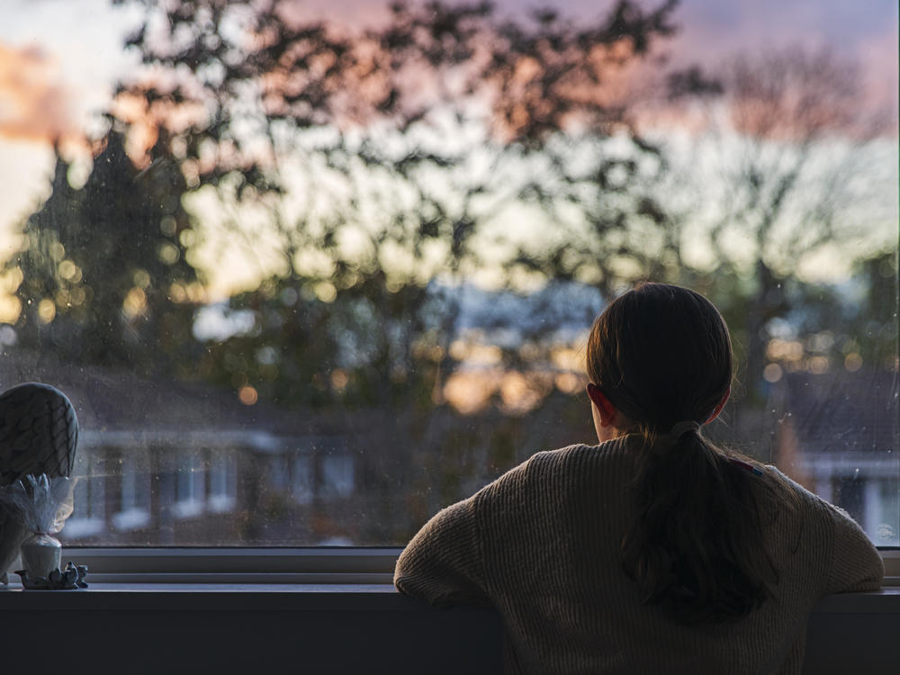 A girl looks out of her bedroom window as the sun is setting.