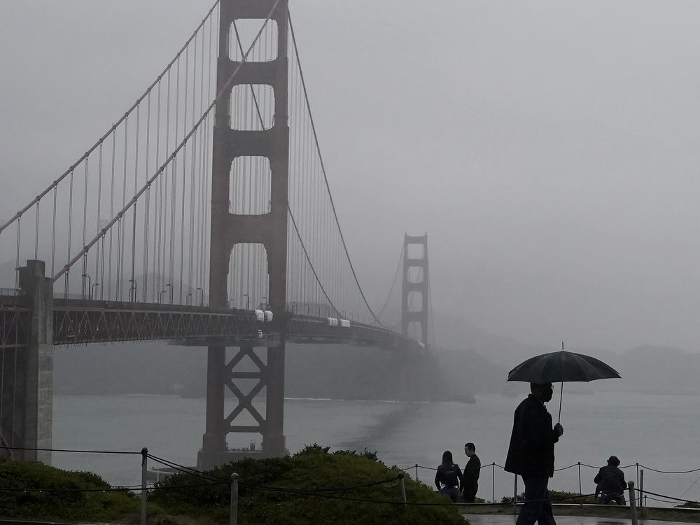 A pedestrian walks with an umbrella near the Golden Gate Bridge in San Francisco during a shower on Wednesday. Strong storms are expected to bring substantial rain to the Western U.S. within the next week.