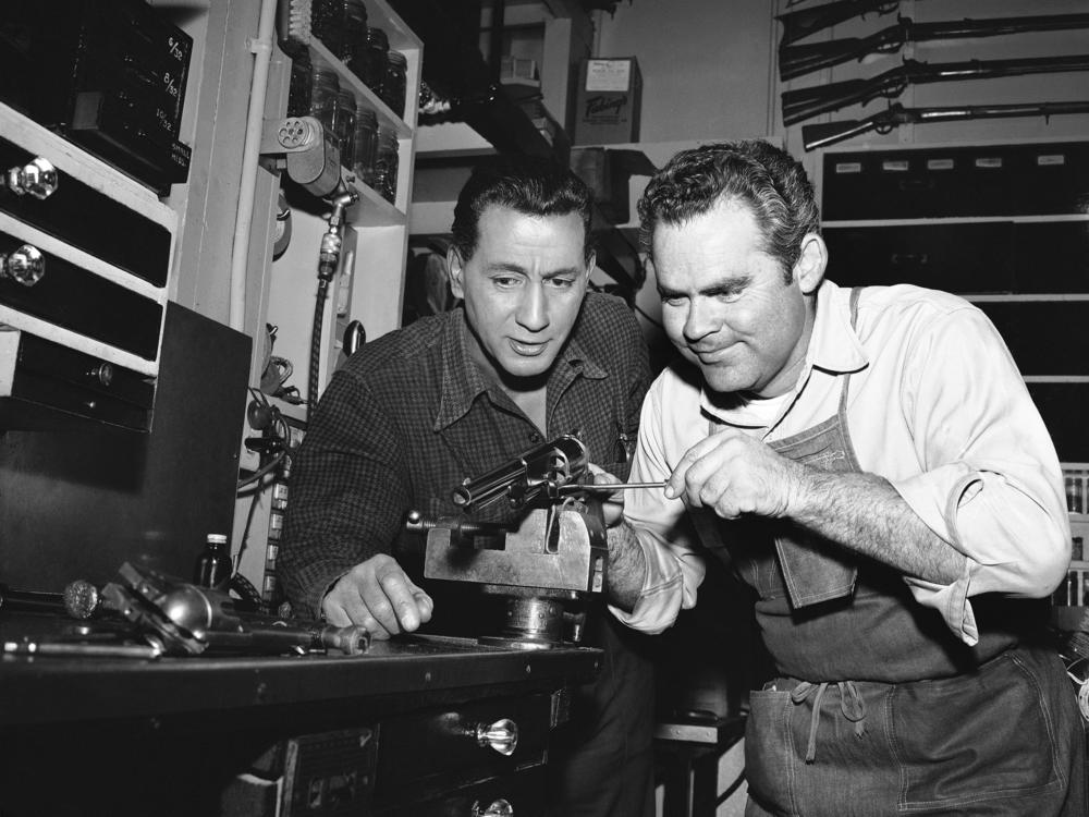 In this photo from a Hollywood studio gun department in 1958, Rodd Redwing (left) checks the final adjustment that Bob Lane is making on a six-gun. Redwing is an actor and a teacher of western gun handling. Lane is one of the men who repair and service the many guns in the studio arsenal.