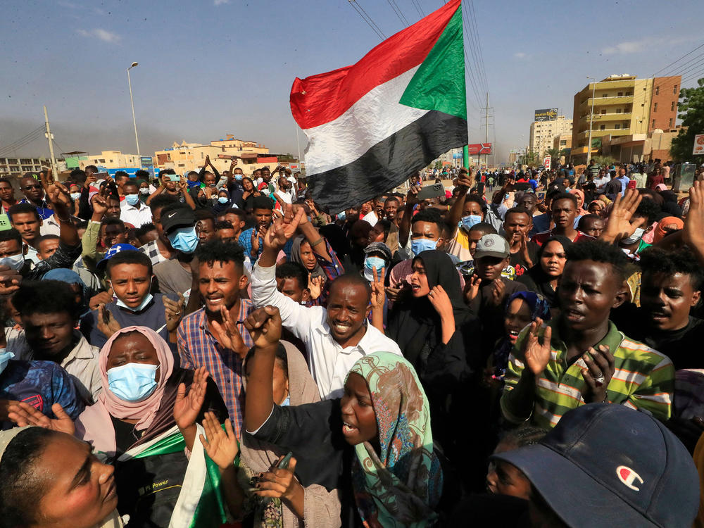 Sudanese protesters lift national flags as they rally on 60th Street in the capital Khartoum, to denounce overnight detentions by the army of government members, on Oct. 25, 2021.