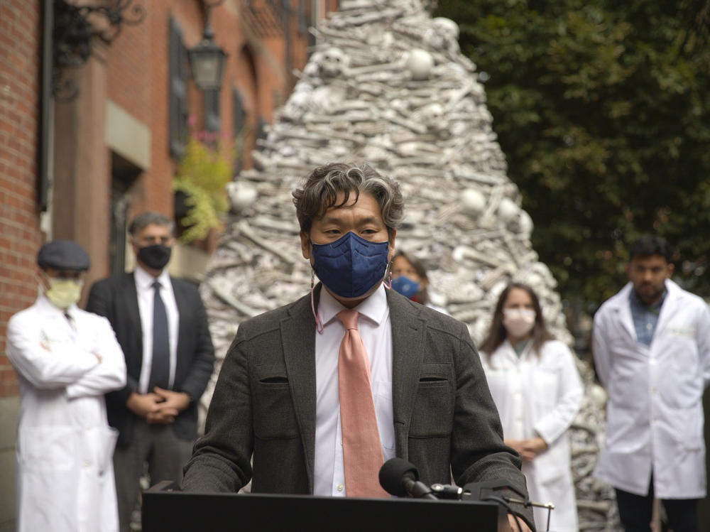 Dr. KJ Seung, a professor at Harvard Medical School, speaks at a September rally outside the home of the CEO of Moderna, maker of one of the two mRNA vaccines that prevent COVID-19. The fake bones are meant to represent lives lost unnecessarily to the coronavirus. Seung was part of a group of doctors demanding Moderna share vaccines — and its recipe — with low-resource countries.
