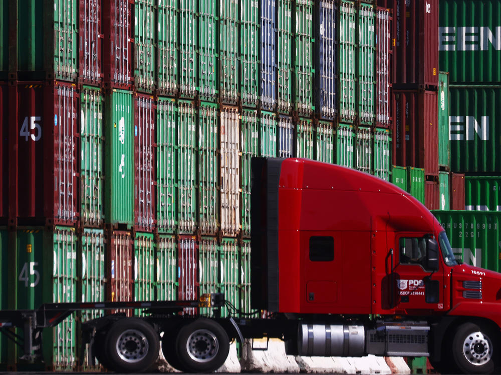 A truck drives past cargo containers stacked at the Port of Los Angeles, the nation's busiest container port, on Oct. 15. Supply chain woes are expected to persist well into next year.