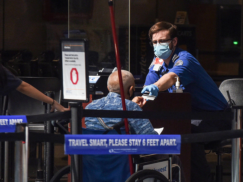 A man using a wheelchair hands his ID to an officer at a security screening checkpoint at Orlando International Airport in 2020.