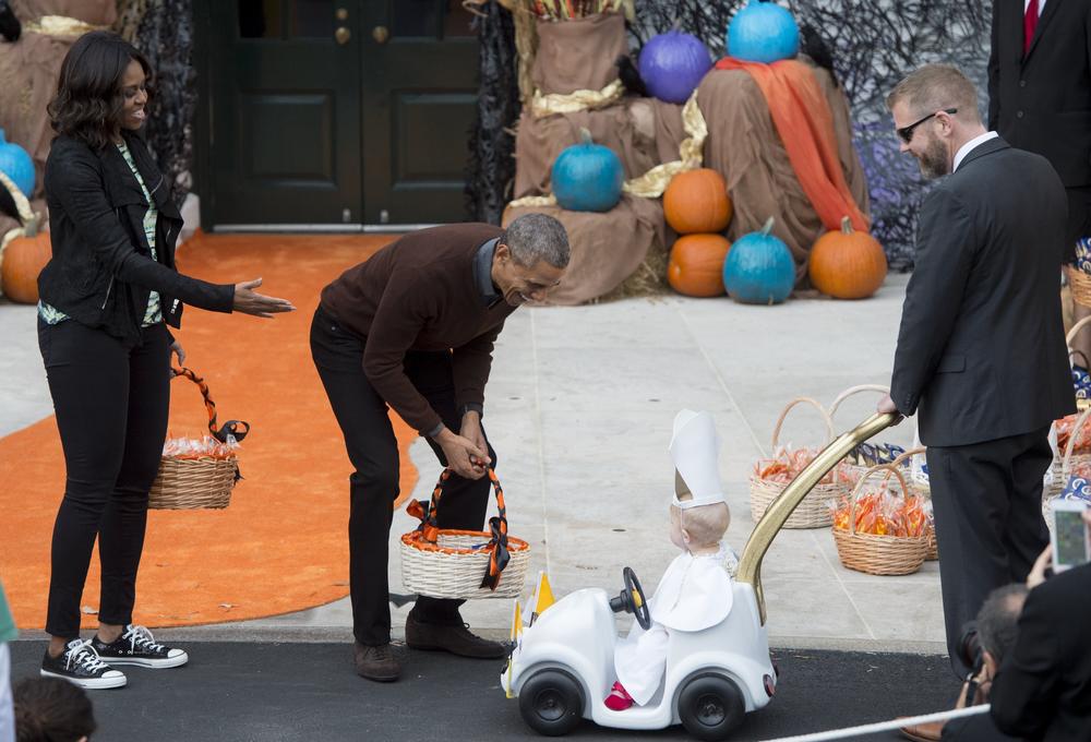 President Barack Obama and First Lady Michelle Obama greet a young child dressed as the Pope and riding in a 