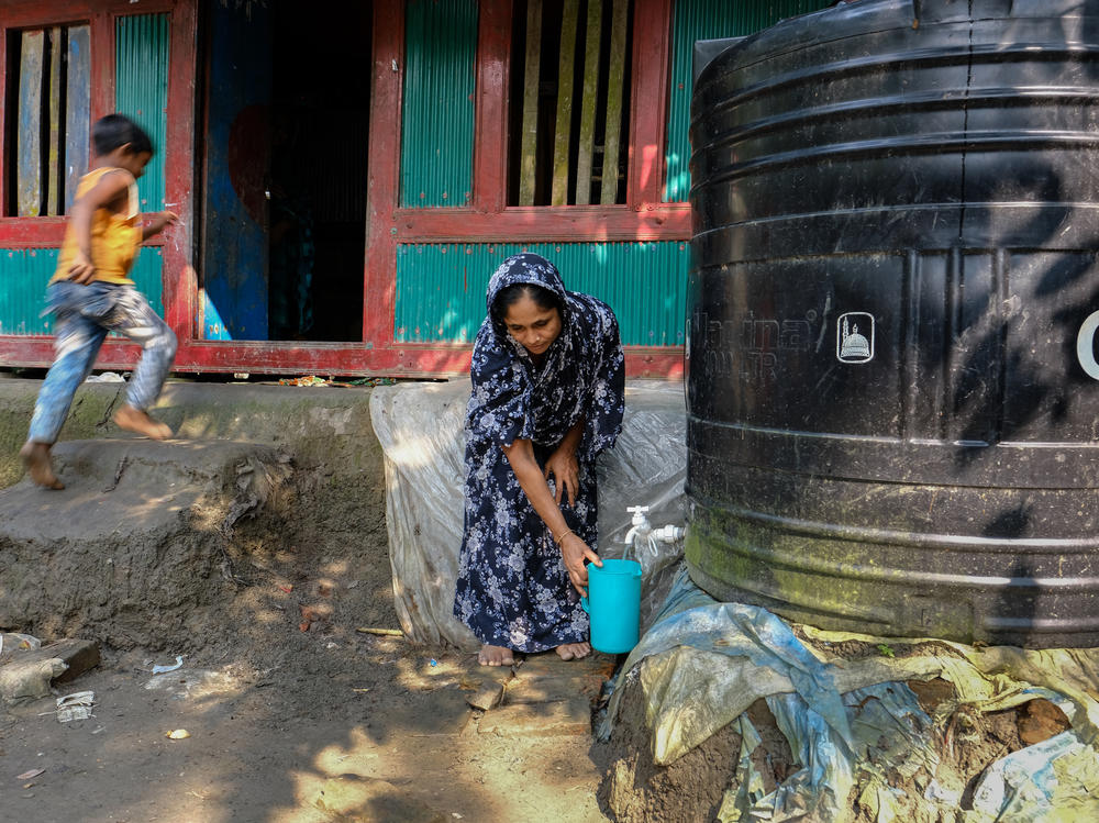 Sitara Begum fills buckets with drinking water from a plastic water tank.