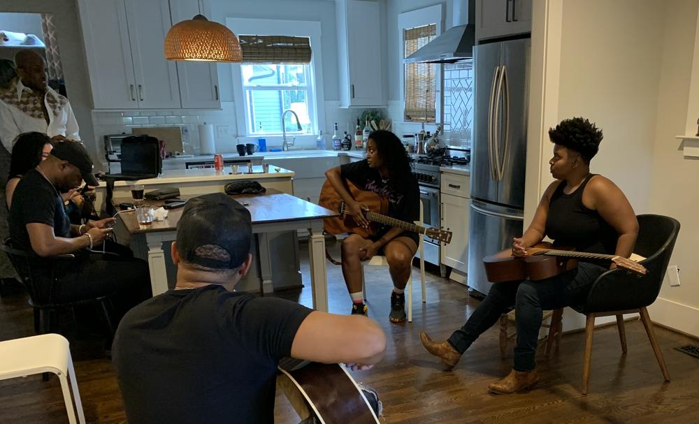 Musicians (including Tylar Bryant, seated in foreground; Roberta Lea, with guitar at table; Joy Clark, right) play in a round at the Black Opry House rented by journalist Marcus Dowling (standing at left) during the 2021 Americana Fest in Nashville