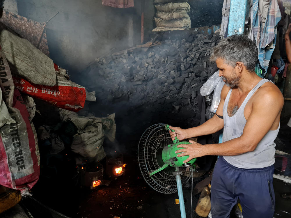 Coal worker Jumman Shaikh aims a fan at a coal-fueled fire inside the Choudhary Coal Depot in Mumbai.