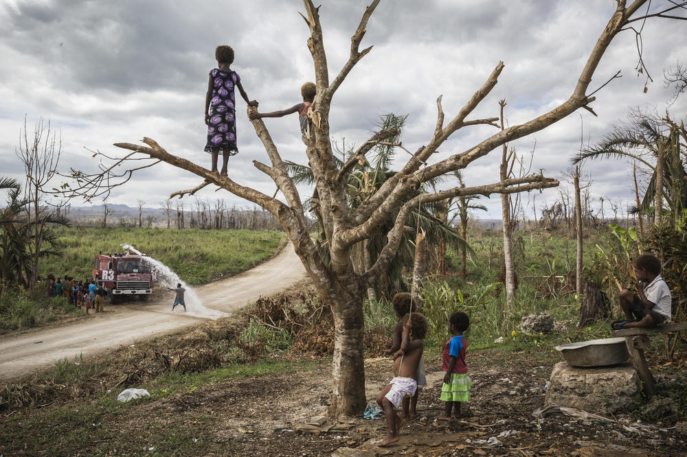Children on Efate island watch a truck delivering drinking water to their village of Etas. After Cyclone Pam hit Vanuatu in March 2015, many local communities were left without fresh water supplies. International charity Oxfam organized an airport water tank truck to come to the villages around Port Vila and help locals to fill their barrels with drinking water.