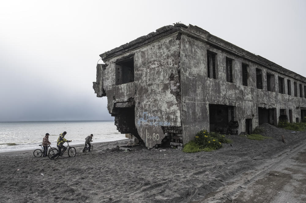 Teenagers ride bikes on the beach next to the destroyed apartment blocks of an area of Oktyabrskiy Settlement that is heavily affected by coastal erosion, in Kamchatka Peninsula, Russia, in 2016. Since the 1970s, the sea has been claiming the land, destroying part of the settlement.