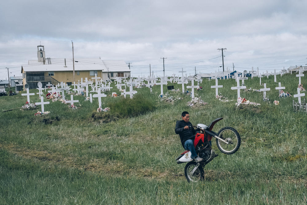 A young man rides by Shishmaref cemetery on his motorcycle. Shishmaref is one of the most climate change-affected settlements in Alaska. Located on a sandbar between the Chukchi Sea and Shishmaref Lagoon, the village has lost significant landmass to rising sea levels and coastal erosion.