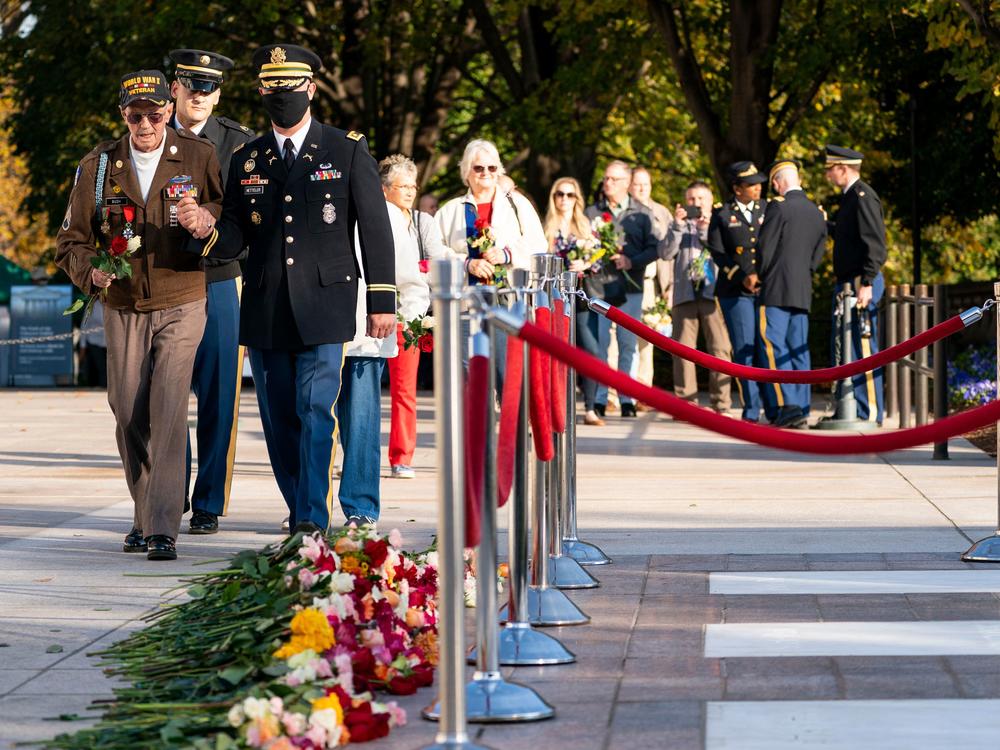 Darrell Bush, age 96, left, a former U.S. Army Staff Sgt. from Camp Springs, Md. and a WWII veteran of the Battle of the Bulge, arrives to place a flower during a centennial commemoration event at the Tomb of the Unknown Soldier in Arlington National Cemetery on Wednesday in Arlington, Va.
