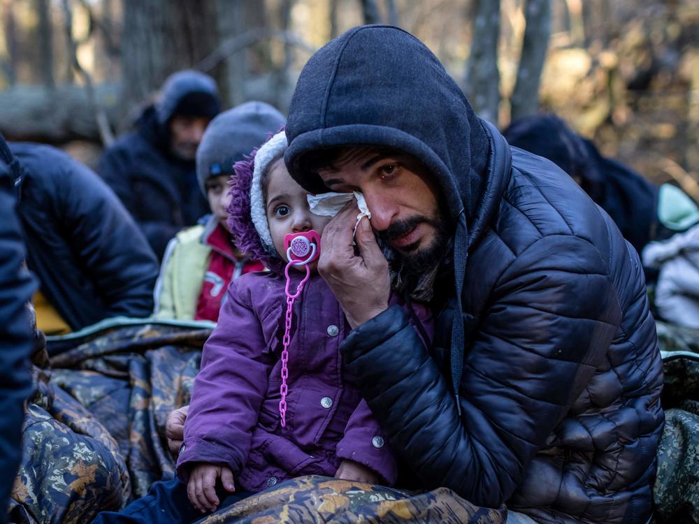 A man holding a child wipes his eye as the Kurdish family from Dohuk in Iraq waits for the border guard patrol, near Narewka, Poland, near the Polish-Belarusian border on Nov. 9. The three-generation family of 16 — with seven minors, including the youngest who is 5 months old — spent about 20 days in the forest and was pushed back to Belarus eight times.