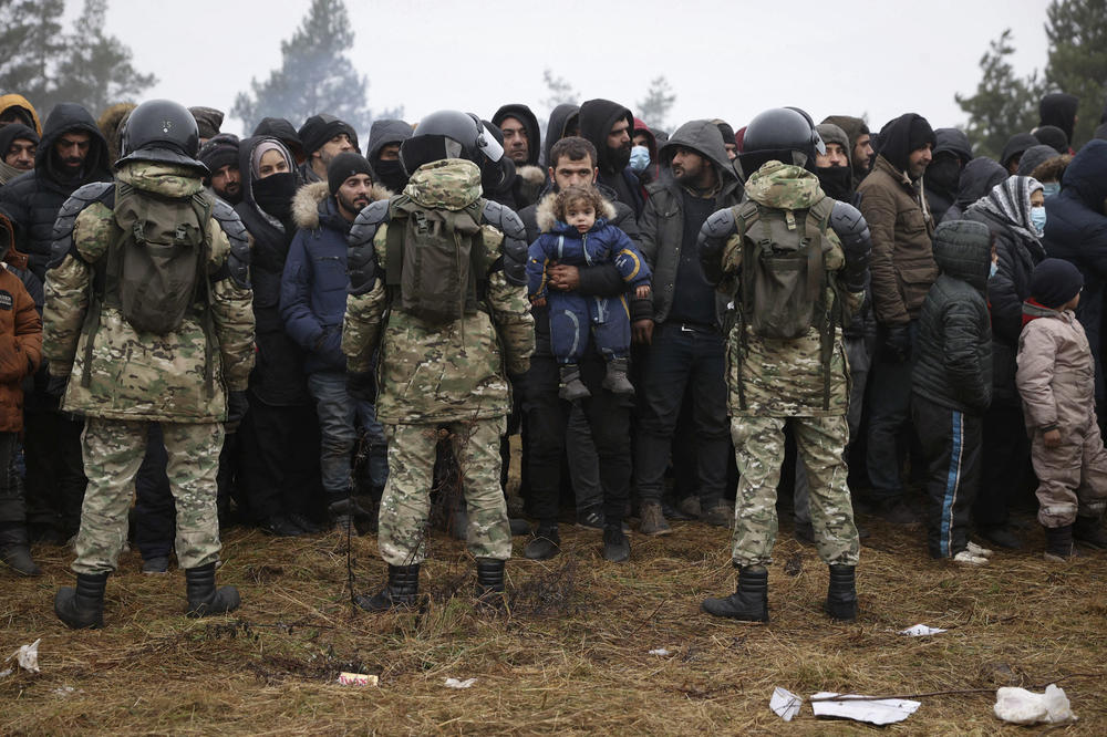 Migrants stand in front of Belarusian servicemen as they gather in a camp near the Belarusian-Polish border in Belarus' Grodno region on Sunday. Polish officials said dozens of migrants were detained that day after crossing into Poland from Belarus.