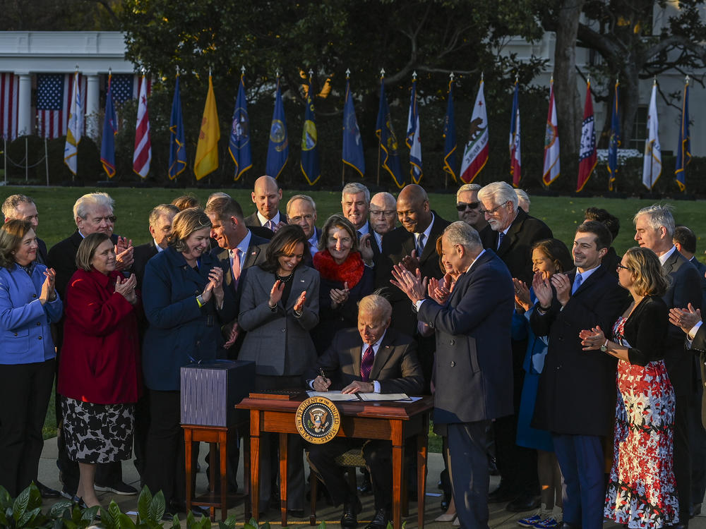 President Biden signs the Infrastructure Investment and Jobs Act as he is surrounded by lawmakers and members of his Cabinet during a ceremony on the South Lawn at the White House on Monday.