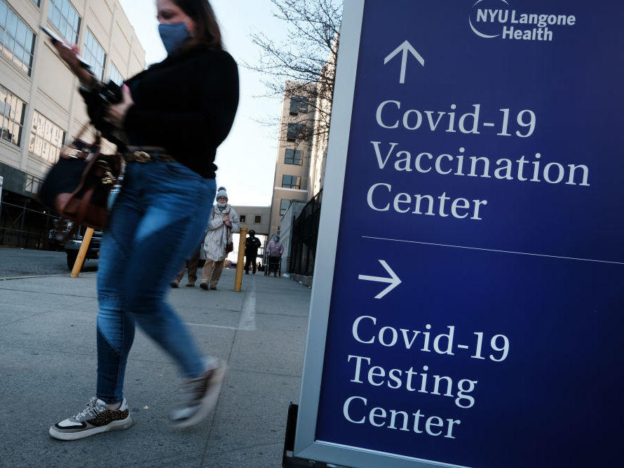People walk by a sign for a COVID-19 testing clinic and a COVID-19 vaccination location outside of a Brooklyn, New York, hospital on March 29.