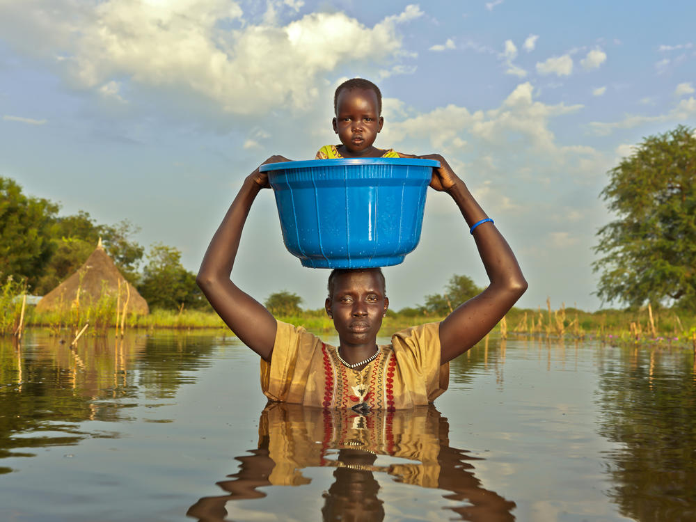 Nyalong Wal, 36, carries her daughter, Nyamal Tuoch, 2, to dry land in a bucket. Mothers do this to protect babies and children from falling into the deep floodwaters, says photographer Peter Caton. (November 2020)