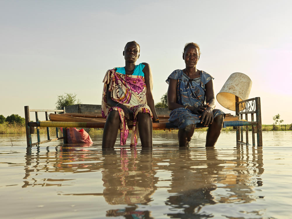 Nyakoang Majok, 28, left, and her mother Nyagout Lok, 46, sit on a bed in the water. (November 2020)