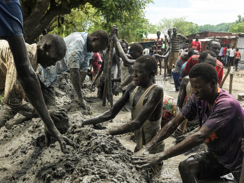 Volunteers build a large dike to contain floodwater that has inundated a soccer field. They are creating a dry area for helicopters carrying emergency aid to land. (September 2021)