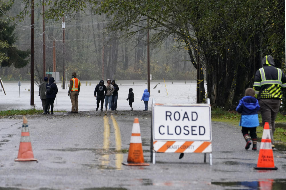 Local residents walk up to a flooded roadway in Sedro-Woolley, Wash., on Monday.