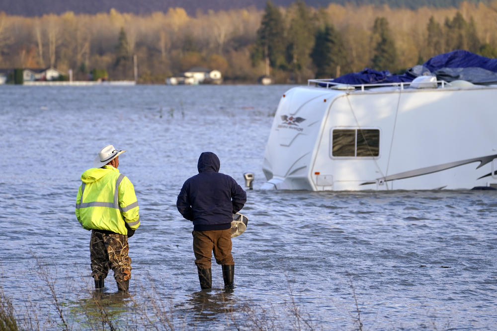 Two men look at a partially submerged recreational vehicle in the flood-swollen Skagit River in Sedro-Woolley, Wash., on Monday.