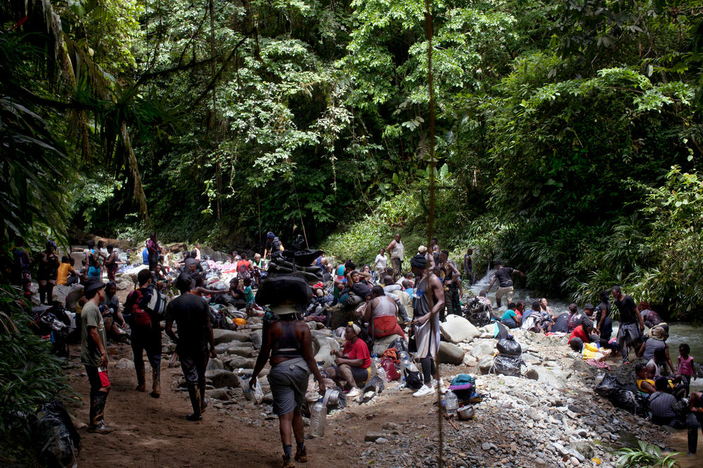 Migrants rest alongside the Acandiseco river after climbing up muddy trails.