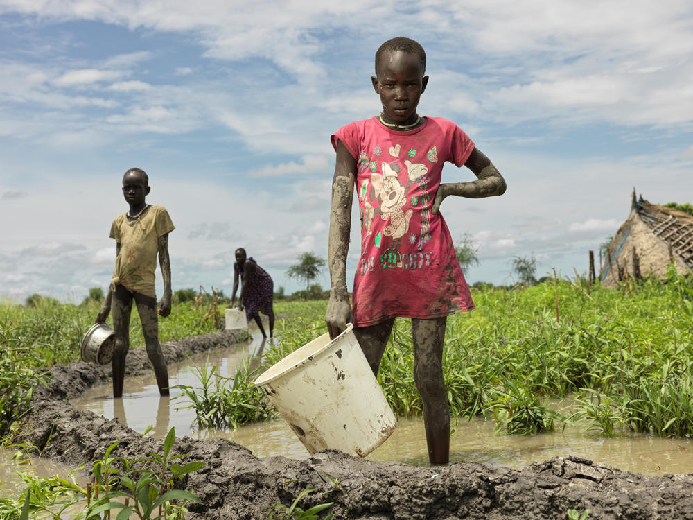 Nyakueni Both, 12, right, tries daily in vain to throw water out of her inundated home with help of her twin sister, Nyagak, left, and mother, Nyayiola Nyuon, 32, center. 