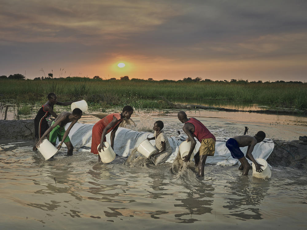 The sun setting behind them, a family works to remove floodwater that gushed into their land after a dike broke just a few hours before, in the village of Old Fangak in Jonglei State, South Sudan. (September 2021)