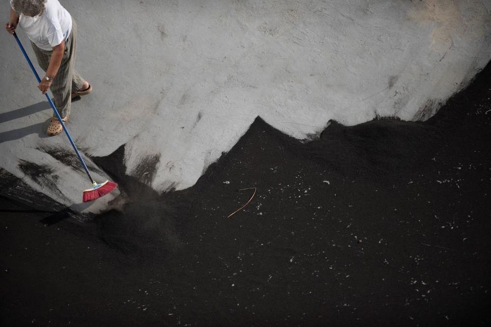 A man sweeps ash spewed by the La Palma volcano off the roof. Authorities say a 72 year old man died while cleaning ash from his home. Residents say the ash has made it difficult to breathe.