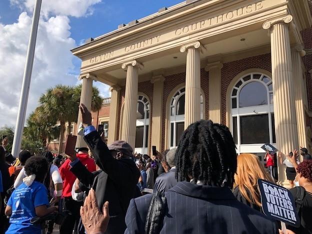 Attendees raise their hands in prayer during a rally outside the Glynn County Courthouse, where the three men accused of murdering Ahmaud Arbery are on trial.