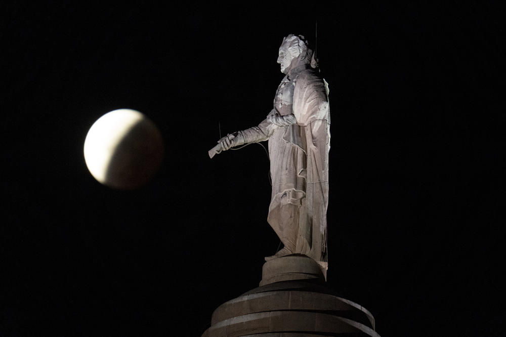 The earth's shadow covers the full moon during a partial lunar eclipse visible near a statue of George Washington atop Baltimore's Washington Monument, on Friday in Baltimore.