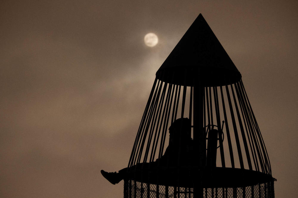 The moon shines though clouds as people sit inside a rocket ship-themed playground tower before a lunar eclipse on Nov. 18 in Torrance, California.
