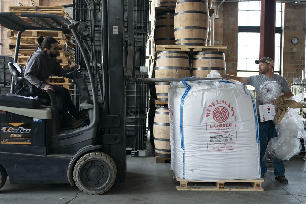Distillery employee Cody Giles, left, uses a forklift to pick up a container of malt.