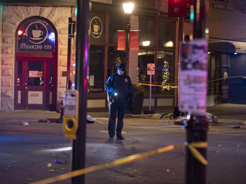 A police officer uses a flashlight while looking for evidence in downtown Waukesha, Wis., after an SUV sped through a barricade and slammed into a Christmas parade Sunday.