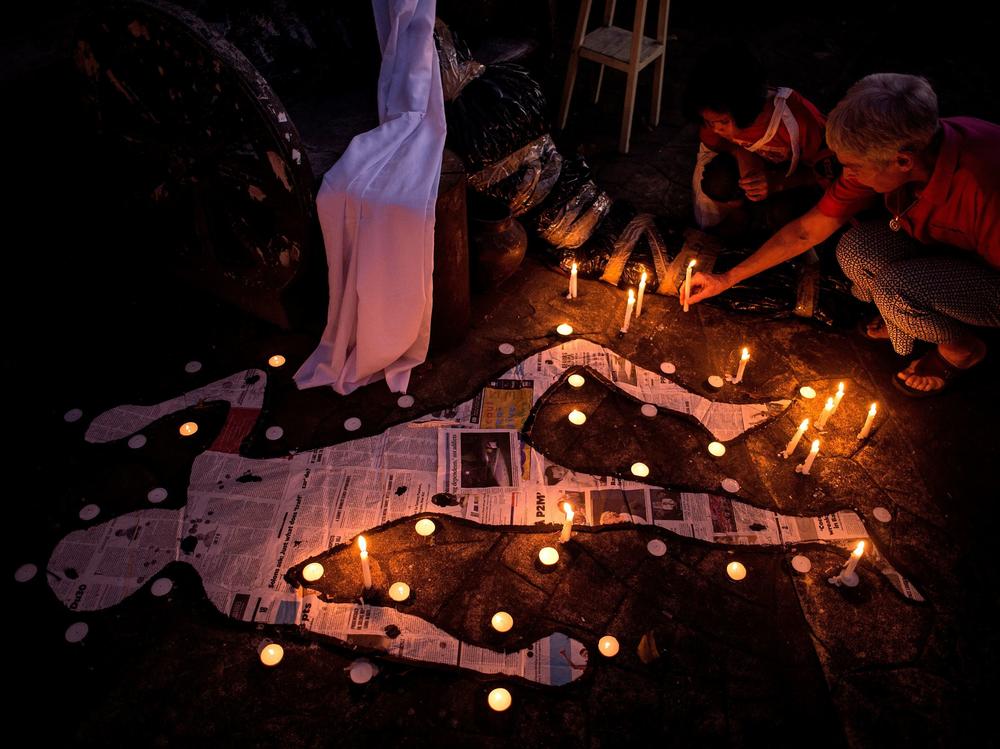 A grandmother and her grandchild light a candle beside mock chalk figure representing an extra judicial killing victim during a prayer rally condemning the government's war on drugs in Manila in 2017.