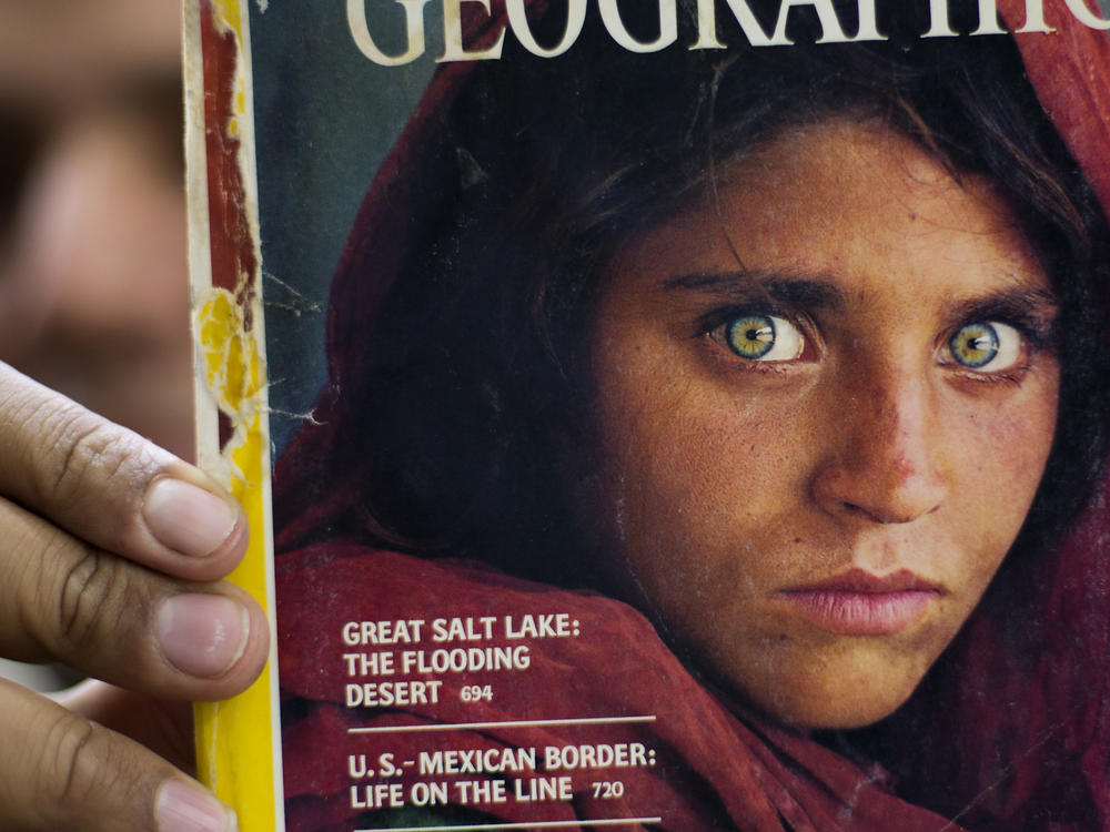 In this file photo from 2016, a bookshop owner in Pakistan shows a National Geographic magazine with the cover photograph of Afghan refugee woman Sharbat Gula. She arrived in Italy as part of the West's evacuation of Afghans following the Taliban takeover of the country, the Italian government said Thursday. The office of Premier Mario Draghi said she asked to be helped to leave the country.