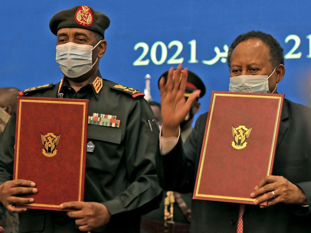 Sudan's top general Abdel Fattah al-Burhan (left) and Prime Minister Abdalla Hamdok lift documents during a deal-signing ceremony to restore the transition to civilian rule in the country in the capital Khartoum, on November 21, 2021.