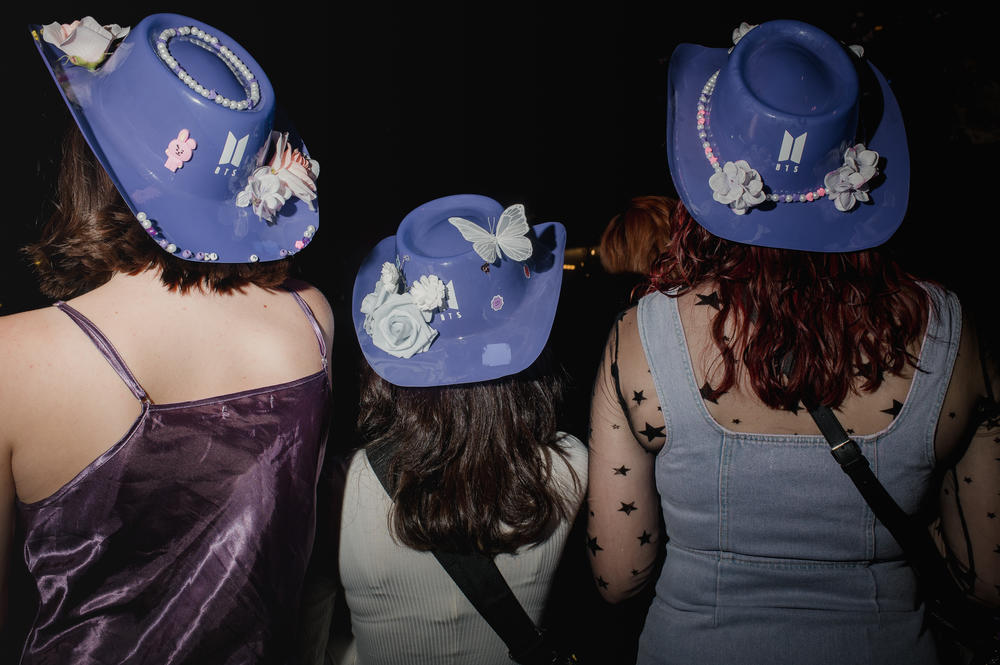 Three fans show off their BTS hats as they wait for the first BTS in person concert in two years.