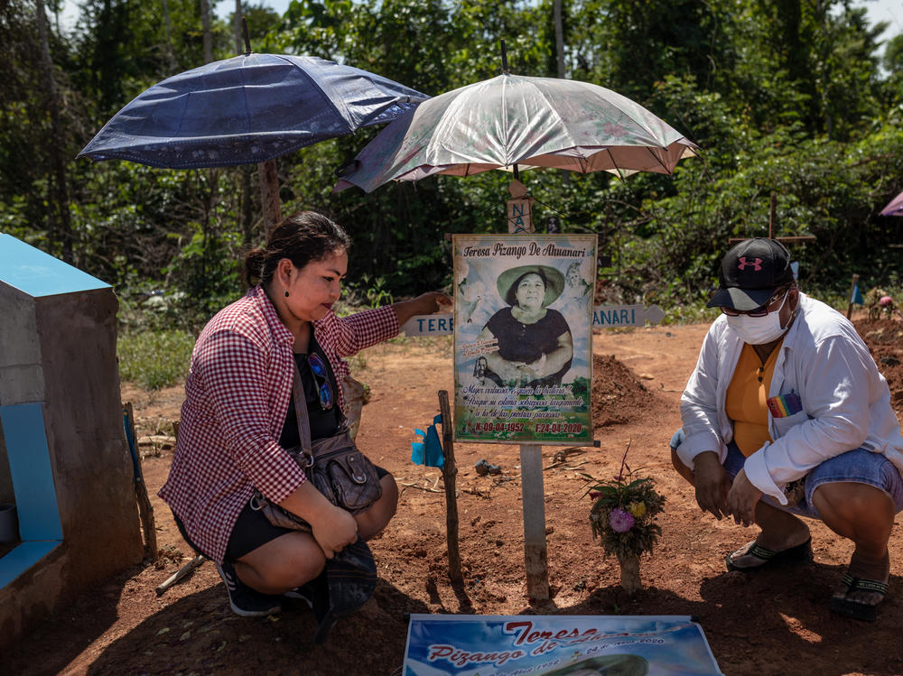 Margarita Ahuanari, left, and Karina Ahuanari look at posters of their mother. The images were placed where they think she was buried at the mass grave that was later renamed the COVID-19 Cemetery in Iquitos.