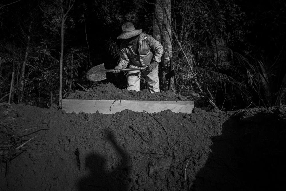 The shadow of a person attending a funeral for someone who died from COVID-19 is cast on a collective grave, while an undertaker works to close the grave under harsh sun in the Nossa Senhora Aparecida cemetery, in western Manaus, on June 5, 2020.