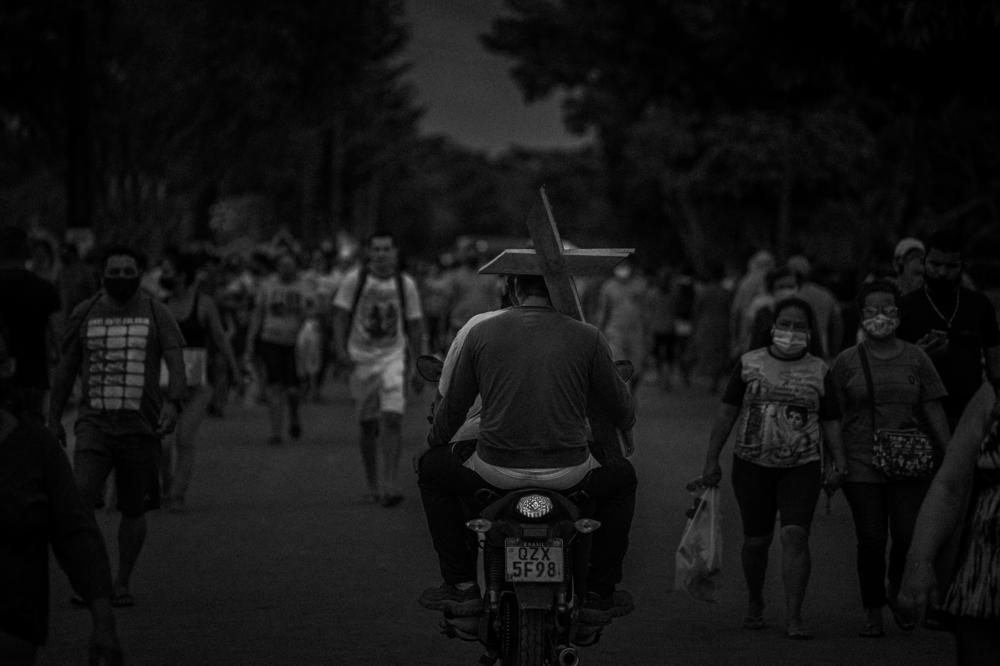 Gravediggers on a motorcycle pass a crowd entering the Nossa Senhora Aparecida Cemetery, as they carry crosses for the Day of Dead in Manaus, on Nov. 2, 2021. The cemetery was designated for mass grave burials during the first coronavirus outbreak the year before. Cemeteries closed when the first cases were reported in the city.