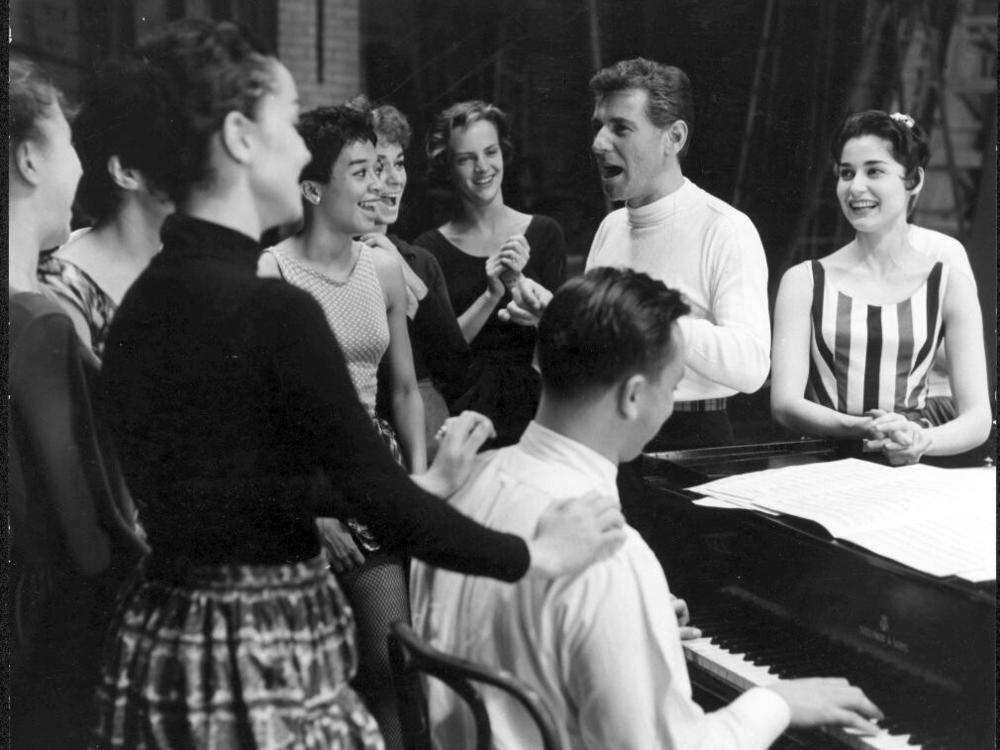 Leonard Bernstein at rehearsal for West Side Story. Carol Lawrence (who played Maria) is at his left, and lyricist Stephen Sondheim is playing the piano, 1957.