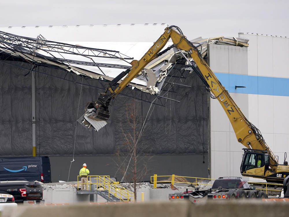 Workers use equipment to remove a section of roof left on a heavily damaged Amazon fulfillment center Saturday in Edwardsville, Ill.