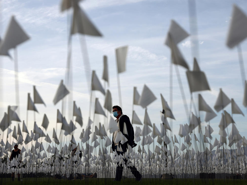 A person wearing a face covering walks past a white flag memorial installation outside Griffith Observatory honoring the nearly 27,000 Los Angeles County residents who have died from COVID-19 on Nov. 18 in Los Angeles, Calif.