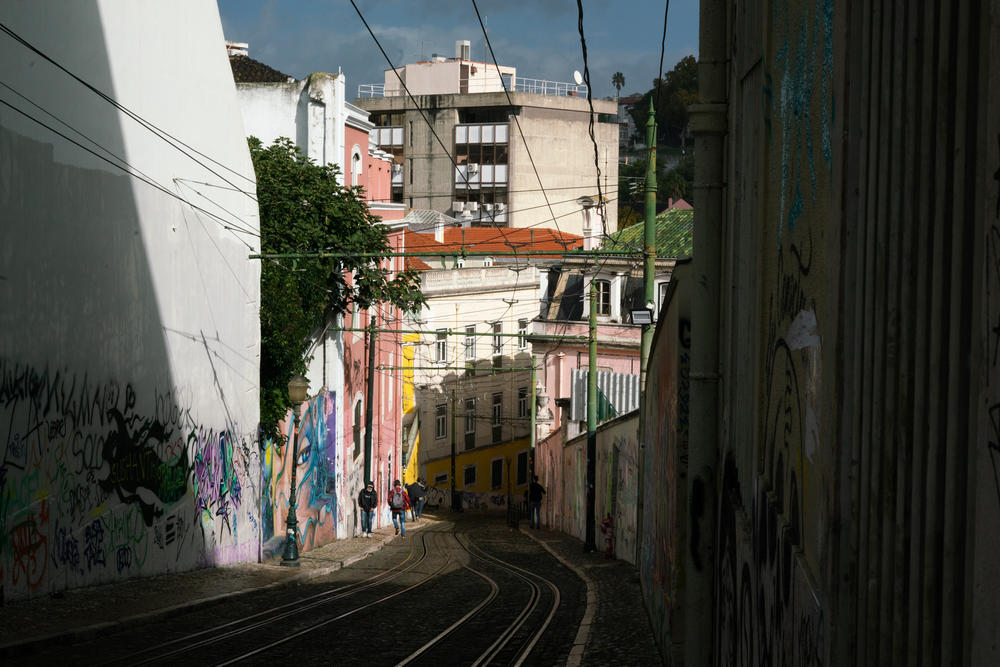 People walk on a steep street next to tracks for the Elevador da Glória in Lisbon, Portugal.