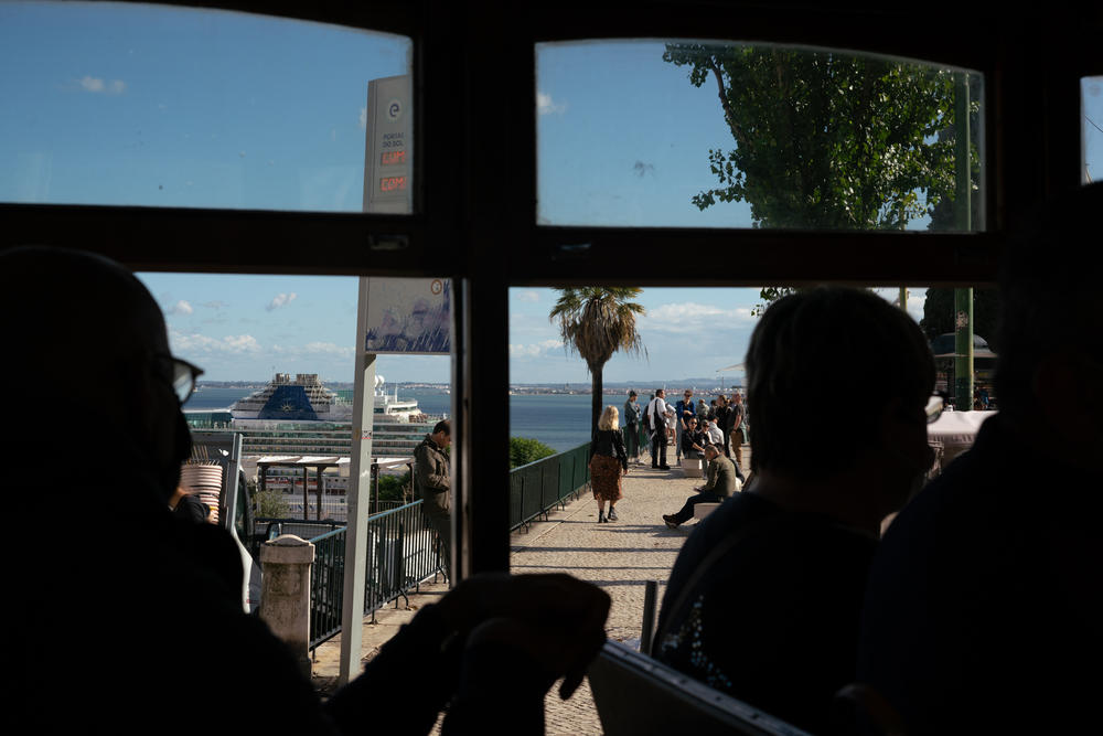 Passengers on Tram 28, a popular and scenic trolley, stare out at people gathered on the seaside in Lisbon, Portugal.